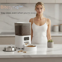 Woman standing in kitchen with BiteSynq™ Smart Automatic Cat Feeder with HD Camera, showing modern design, 5L capacity, and food bowl for cats and dogs.
